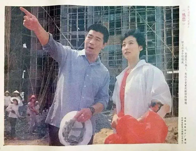 剧照：一名男子抬手指向远方，身旁女子随他望去，两人身后是脚手架林立的建筑工地，工人在下方劳作。